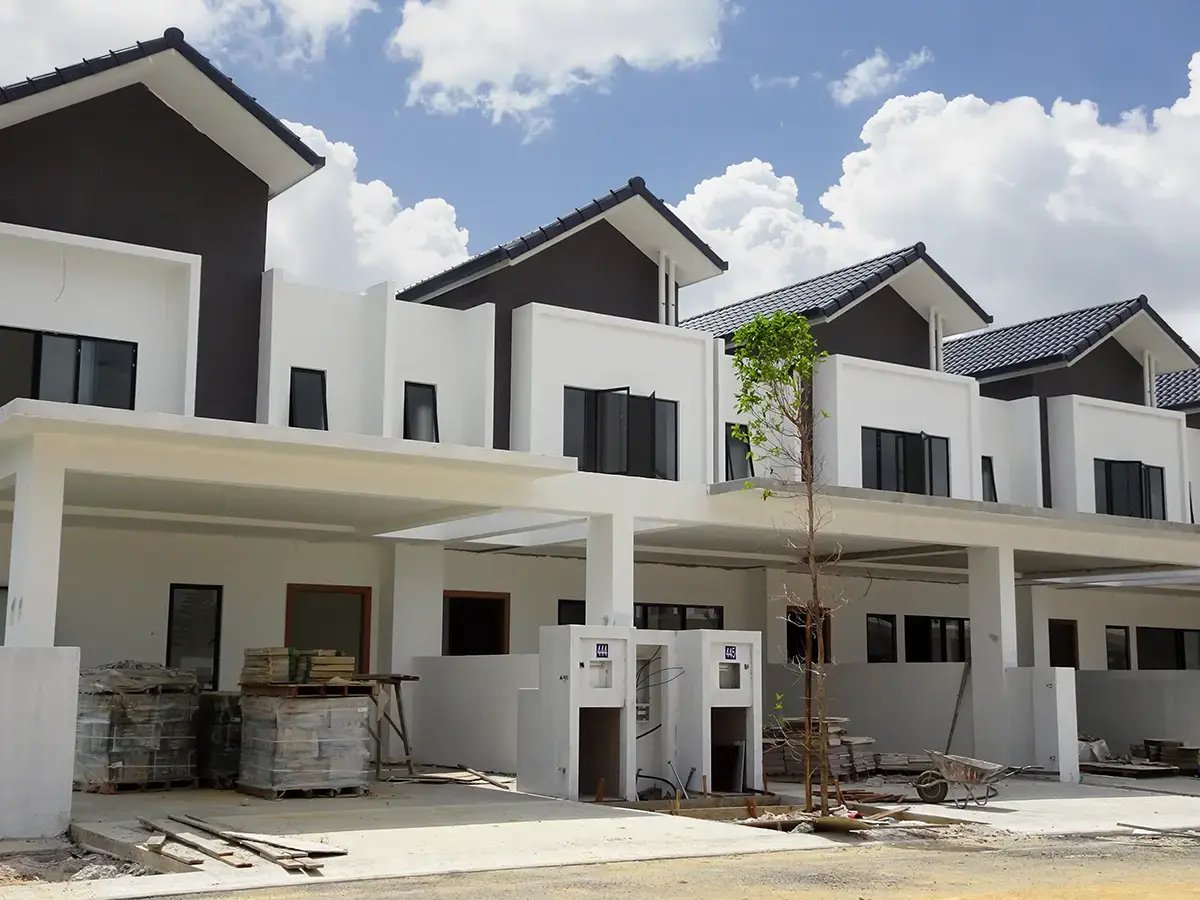 Row of modern white townhouses under a cloudy blue sky, with a lone tree and construction materials in the foreground